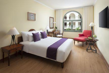 Interior view of the Superior Room with Queen bed, bedside tables, armchair, TV and window overlooking courtyard