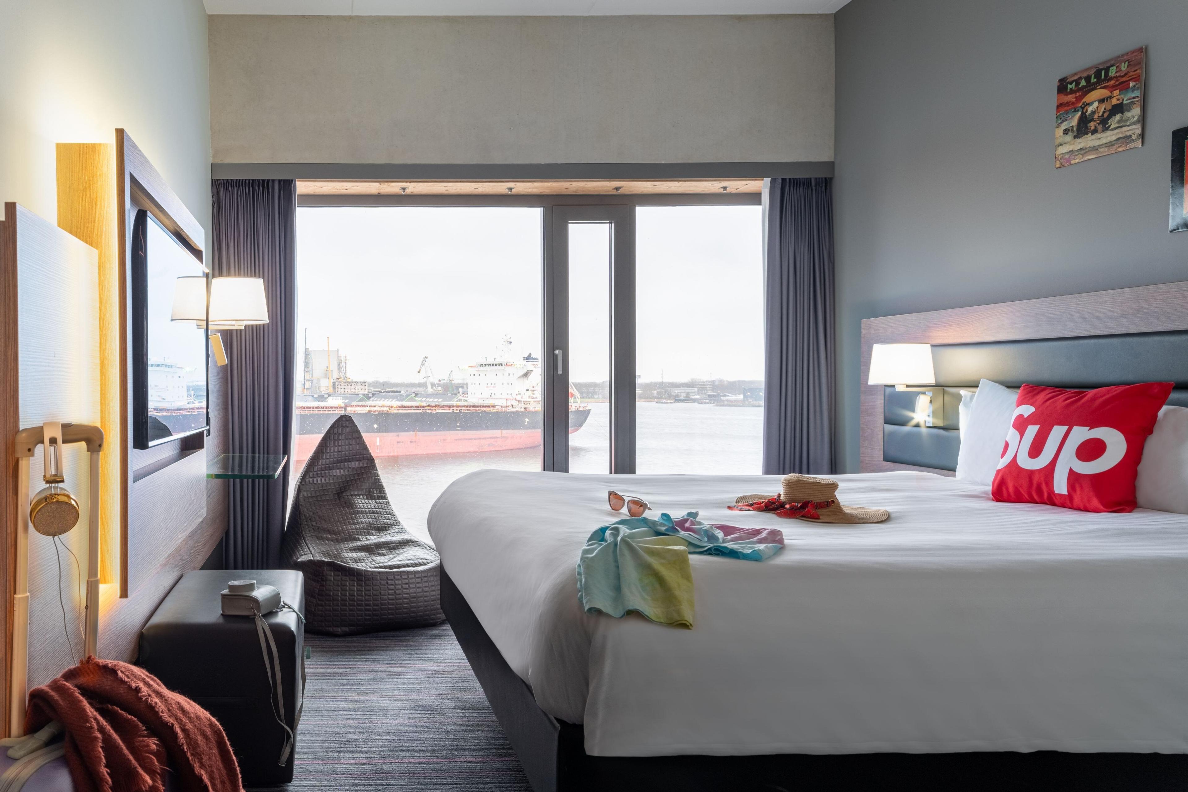 Moxy Sleeper Lookout Queen rooms boast breathtaking views of the Amsterdam harbor scene through dramatic floor to ceiling windows.