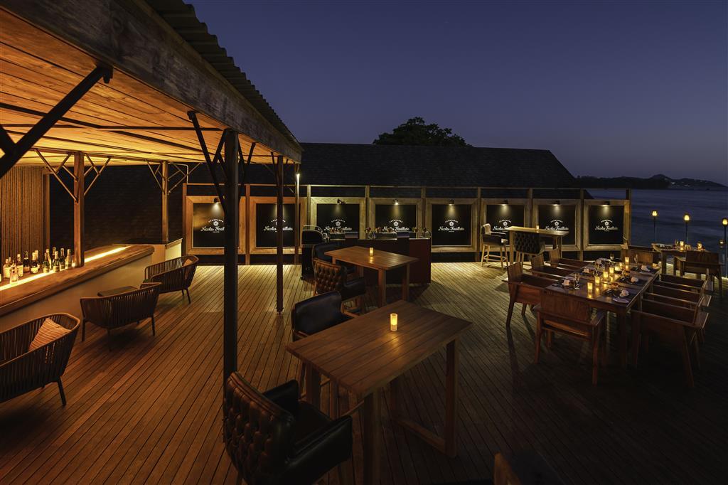 Exterior view of outdoor seating and bar area at The Terraces Restaurant with ocean view at night